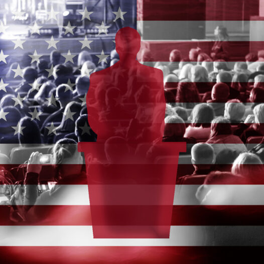 Silhouette of a male politician at a podium. Background shows a diverse crowd of people sitting in an auditorium, embossed over an image of the United States flag.