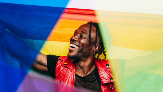 Black man smiling overlaid with pride flags and rainbow colors.