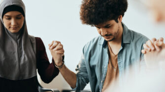 Man holding hands in prayer with woman in head scarf.