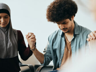 Man holding hands in prayer with woman in head scarf.